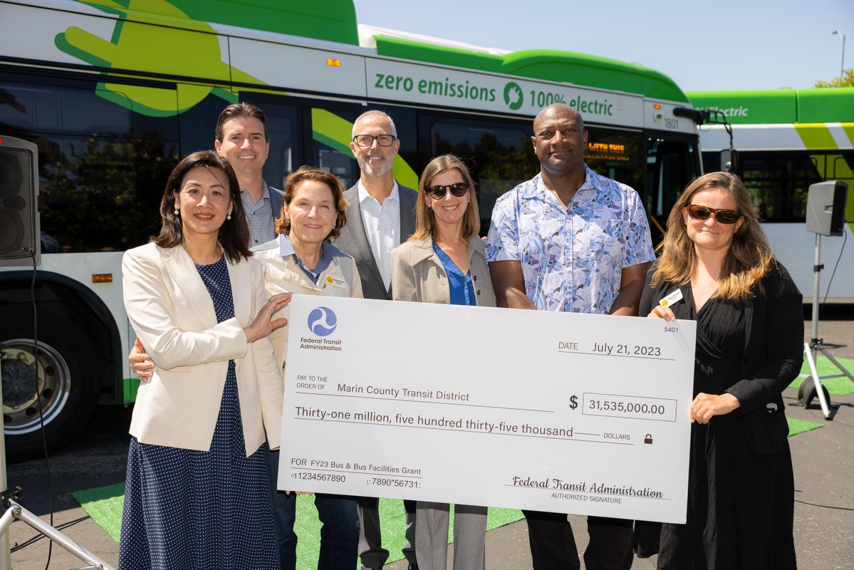 Rep Huffman stands in front of electric bus with large check